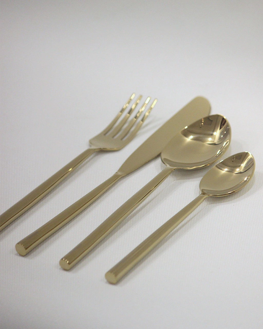 Set of gold-colored cutlery including a fork, knife, and two spoons on decorative table .