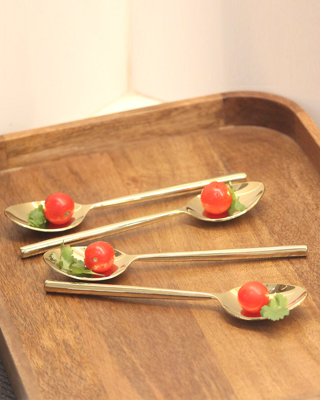 Set of four silver spoons with cherry tomatoes on a wooden tray