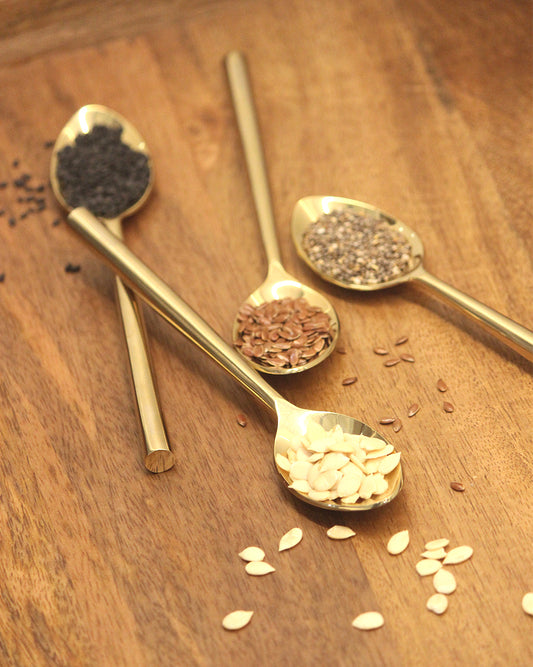 Close-up of a mirror-finish gold spoon holding pumpkin seeds, emphasizing the elegant metallic shine.